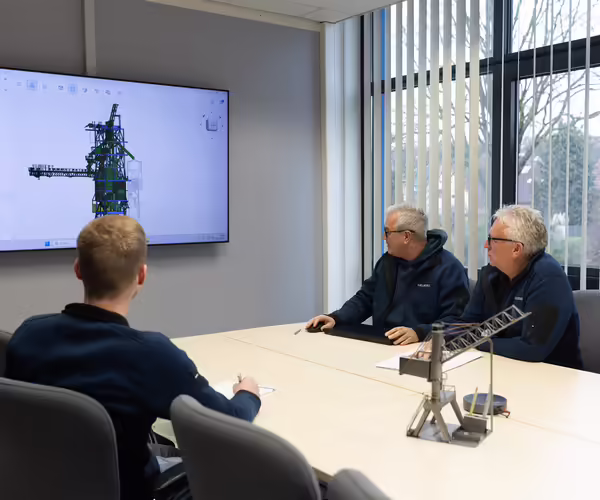 Eine Gruppe NEUERO Mitarbeiter schauen gemeinsam auf ein 3D-Produktmodell, das an die Wand eines Konferenzraumes projeziert wird.