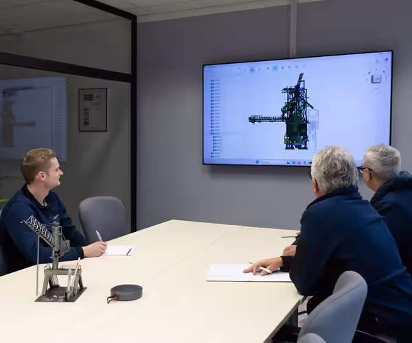 Eine Gruppe NEUERO Mitarbeiter schauen gemeinsam auf ein 3D-Produktmodell, das an die Wand eines Konferenzraumes projeziert wird.