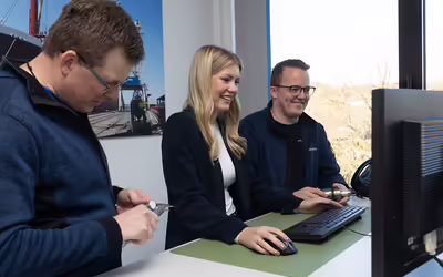 Drei NEUERO Mitarbeiter stehen lächelnd vor einem Bildschirm.