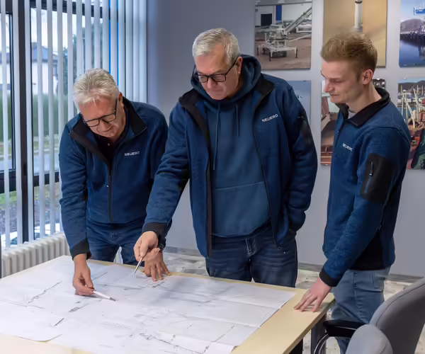 Drei NEUERO Mitarbeiter begutachten eine grosse Skizze, die vor Ihnen auf einem Schreibtisch liegt.