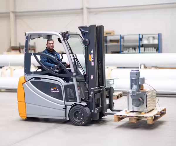 Ein NEUERO Mitarbeiter transportiert ein Maschinenteil mit einem Gabelstapler.