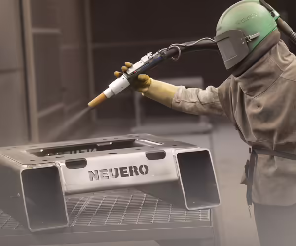 Ein NEUERO Mitarbeiter in Schutzkleidung lackiert ein Metallbauteil.