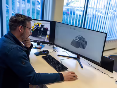 Ein NEUERO Mitarbeiter arbeitet konzentriert am Schreibtisch, auf dem Bildschirm vor ihm ein 3D-Modell eines Maschinenteils. 