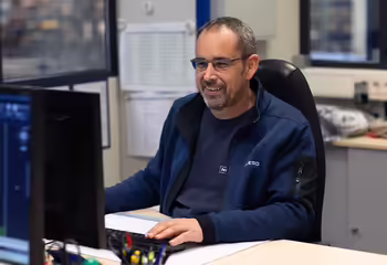 Ein NEUERO Mitarbeiter sitzt lächelnd vor einem Bildschirmarbeitsplatz.